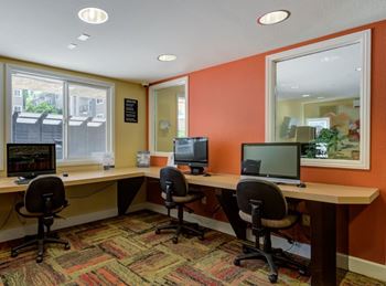 A room with orange walls has a desk with two chairs and two computers on it.